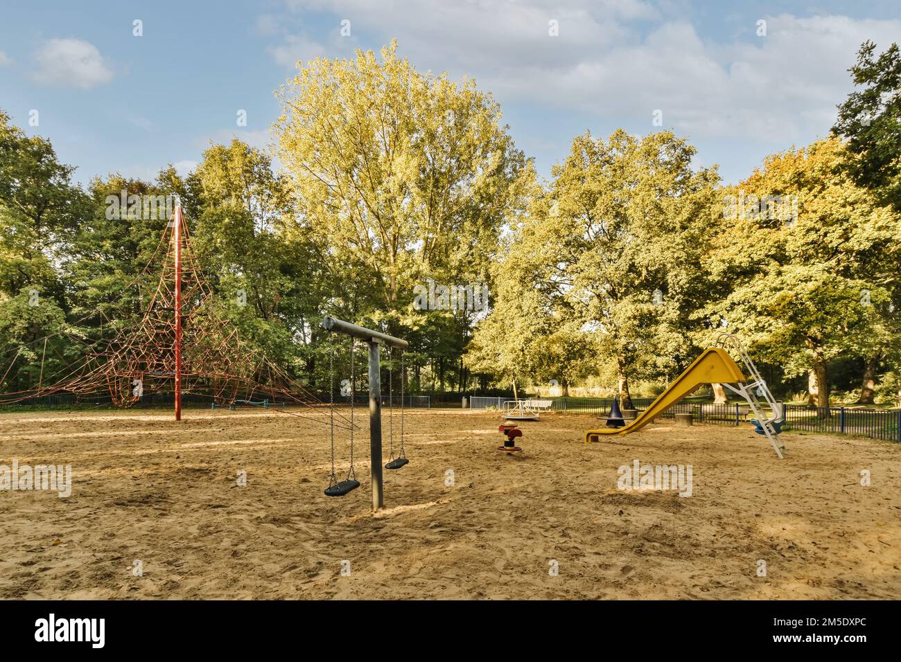 a playground with swings, slides and slides on the ground in front of trees that are turning to yellow leaves Stock Photo