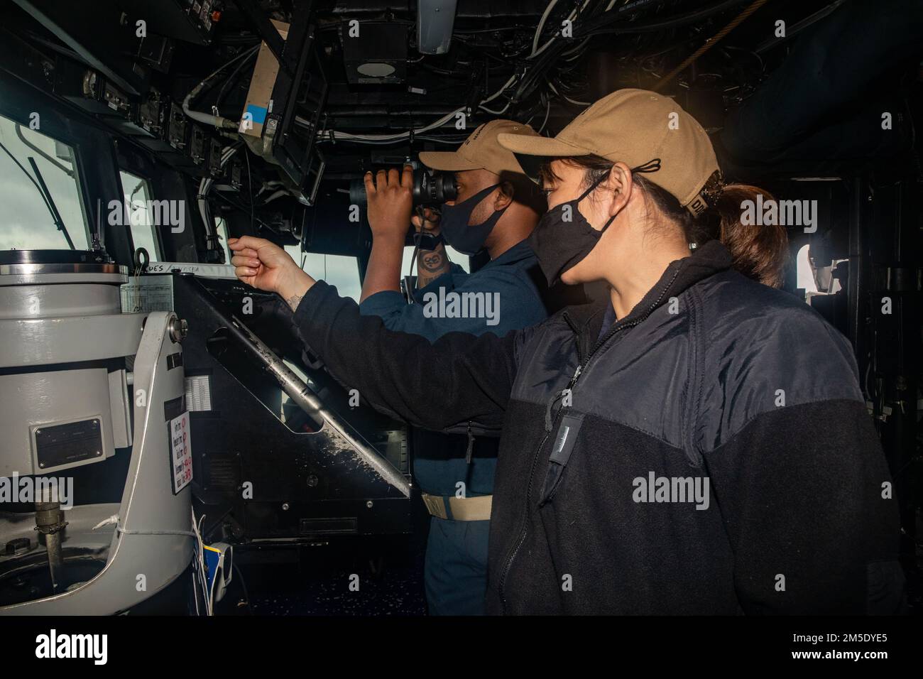 PHILIPPINE SEA (March 5, 2022) Lt.j.g. Valerie Doan (right), from Walnut Creek, Calif., and Ensign Treyvon Darby, from Norfolk, Va., search for surface contacts while standing watch on the bridge aboard Arleigh Burke-class guided-missile destroyer USS Ralph Johnson (DDG 114). Ralph Johnson is assigned to Task Force 71/Destroyer Squadron (DESRON) 15, the Navy’s largest forward-deployed DESRON and the U.S. 7th fleet’s principal surface force. Stock Photo