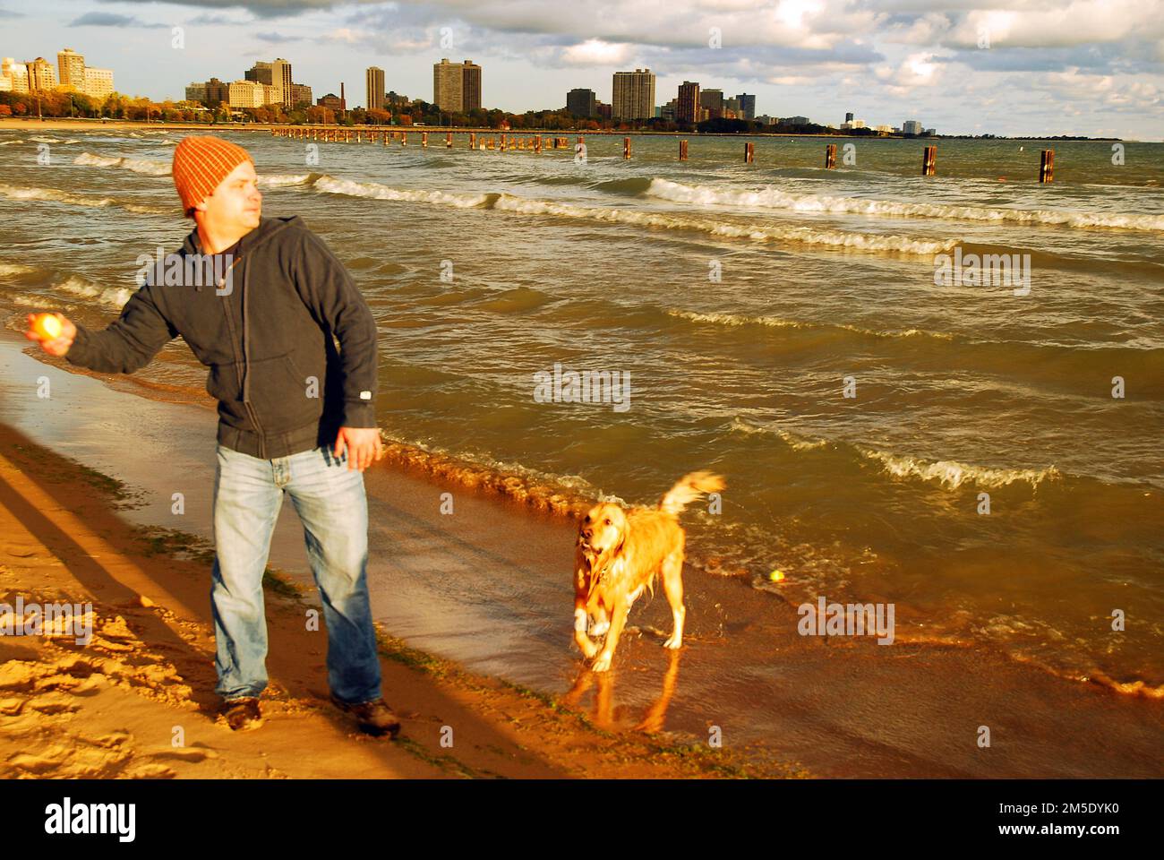 An adult man plays fetch with his dog along the shores of Lake Michigan, Chicago on a chilly autumn day Stock Photo