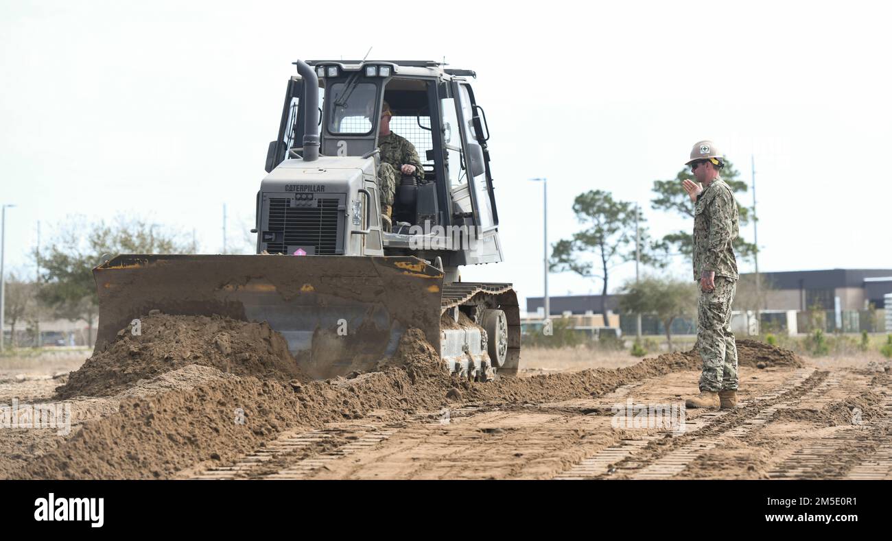 (220305-N-OI810-0350) GULFPORT, Mississippi (March 5, 2022) Construction Mechanic 2nd Class Bradley Damitz, from Virginia Beach, Virginia, assigned to Naval Mobile Construction Battalion (NMCB) 14, guides Logistics Specialist 1st Class Donovan Amos, from Knoxville, Tennessee, assigned to NMCB-14, as he operates a dozer during a berm building simulation during fiscal year 2022, quarter two, Regional Training Platform (RTP-2) at Camp Shelby Joint Forces Training Center, March 5, 2022. RTP-2 provided NMCB-14 Seabees hands-on training opportunities in TCCC; maintenance and material management; civ Stock Photo