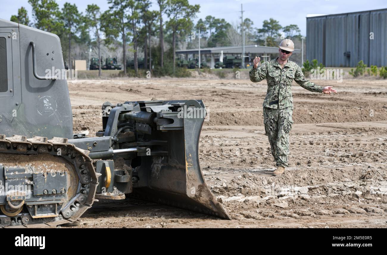 (220305-N-OI810-0307) GULFPORT, Mississippi (March 5, 2022) Construction Mechanic 2nd Class Bradley Damitz, from Virginia Beach, Virginia, assigned to Naval Mobile Construction Battalion (NMCB) 14, guides a dozer operator during a berm building simulation during fiscal year 2022, quarter two, Regional Training Platform (RTP-2) at Camp Shelby Joint Forces Training Center, March 5, 2022. RTP-2 provided NMCB-14 Seabees hands-on training opportunities in TCCC; maintenance and material management; civil engineering support equipment operations; convoy operations; construction operations; combat ope Stock Photo