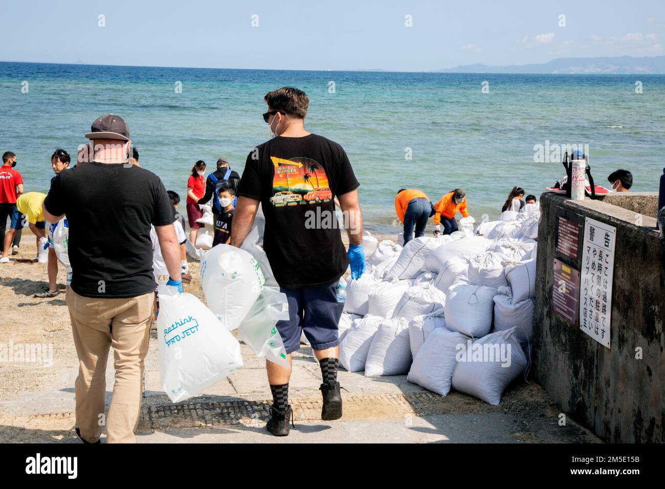 Marines with bags head out to the beach for pumice cleanup, walking by the piles of bags which were already gathered in previous cleanups. Stock Photo