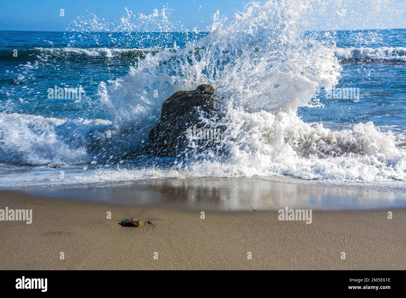 A closeup shot of blue sea waves splashing against a rock on a beach ...