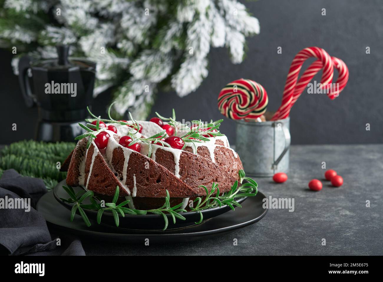 Christmas chocolate bundt cake. Traditional Christmas fruit cake with white glaze, cranberries and rosemary on dark backgroundChristmas decoration. Wi Stock Photo
