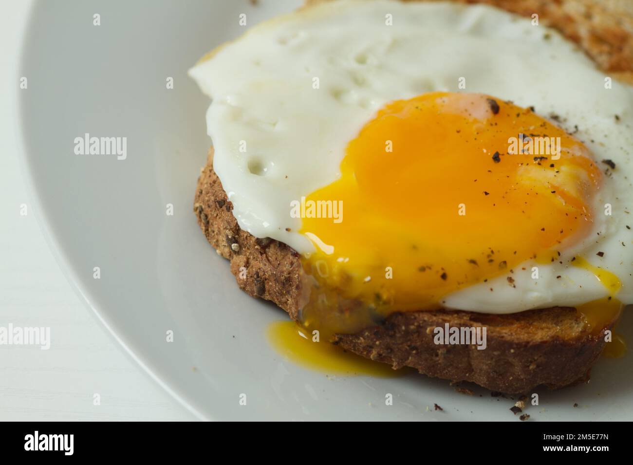 Fried egg on a slice of toasted seeded bread with black pepper sprinkled on top Stock Photo