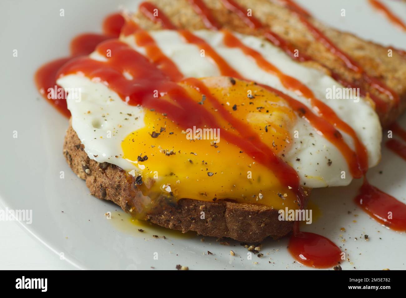 Fried egg on a slice of toasted seeded bread with black pepper and tomato ketchup on top Stock Photo