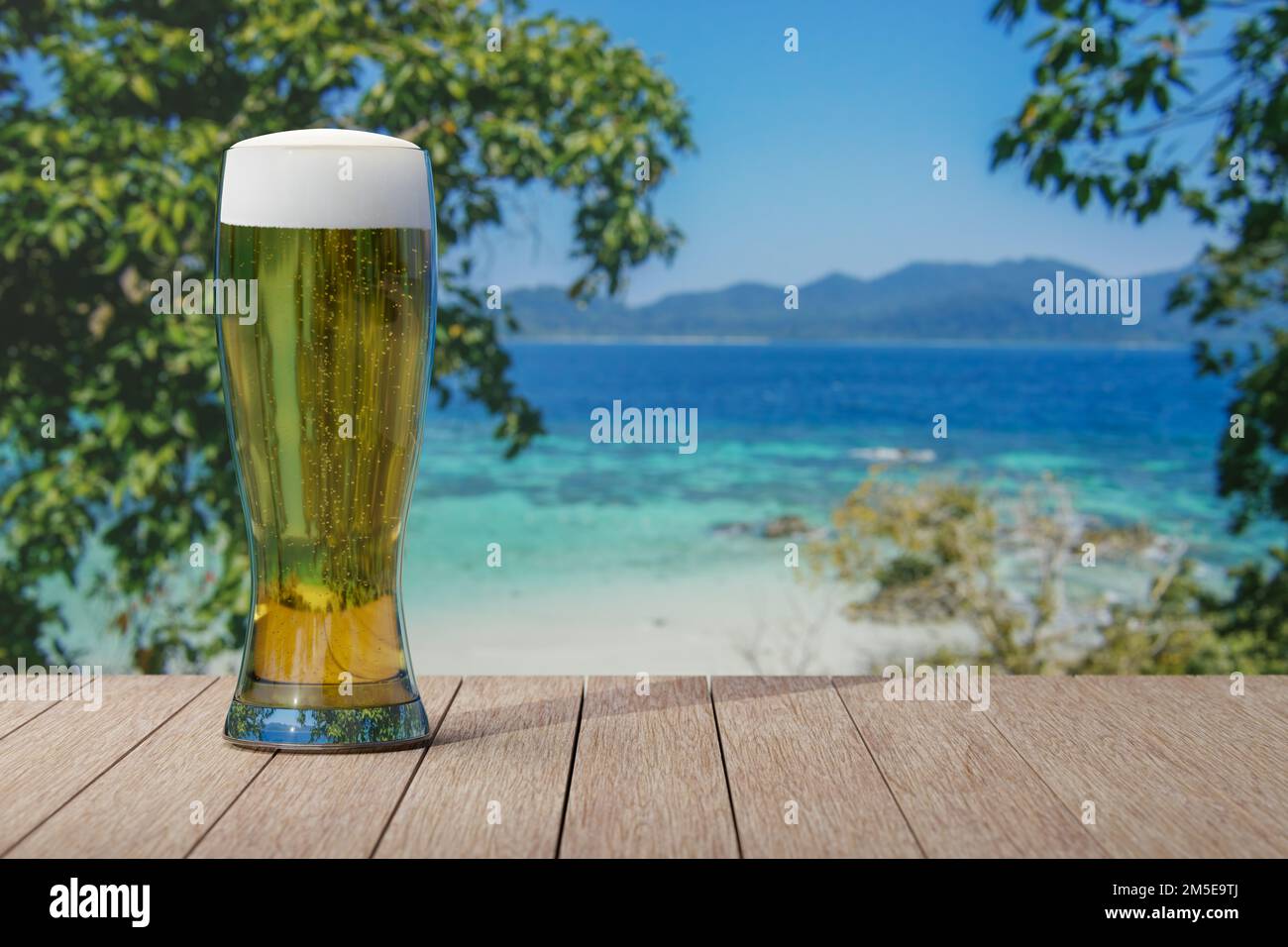 Glass of light beer on table with view of beautiful beach and sea with turquoise water. Stock Photo