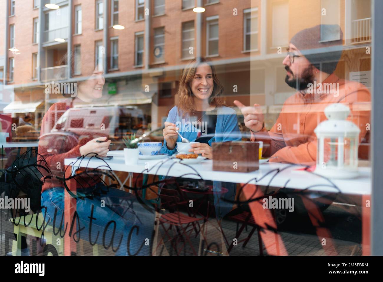 Three young people sitting at a cafe, smiling, and having a warm conversation Stock Photo