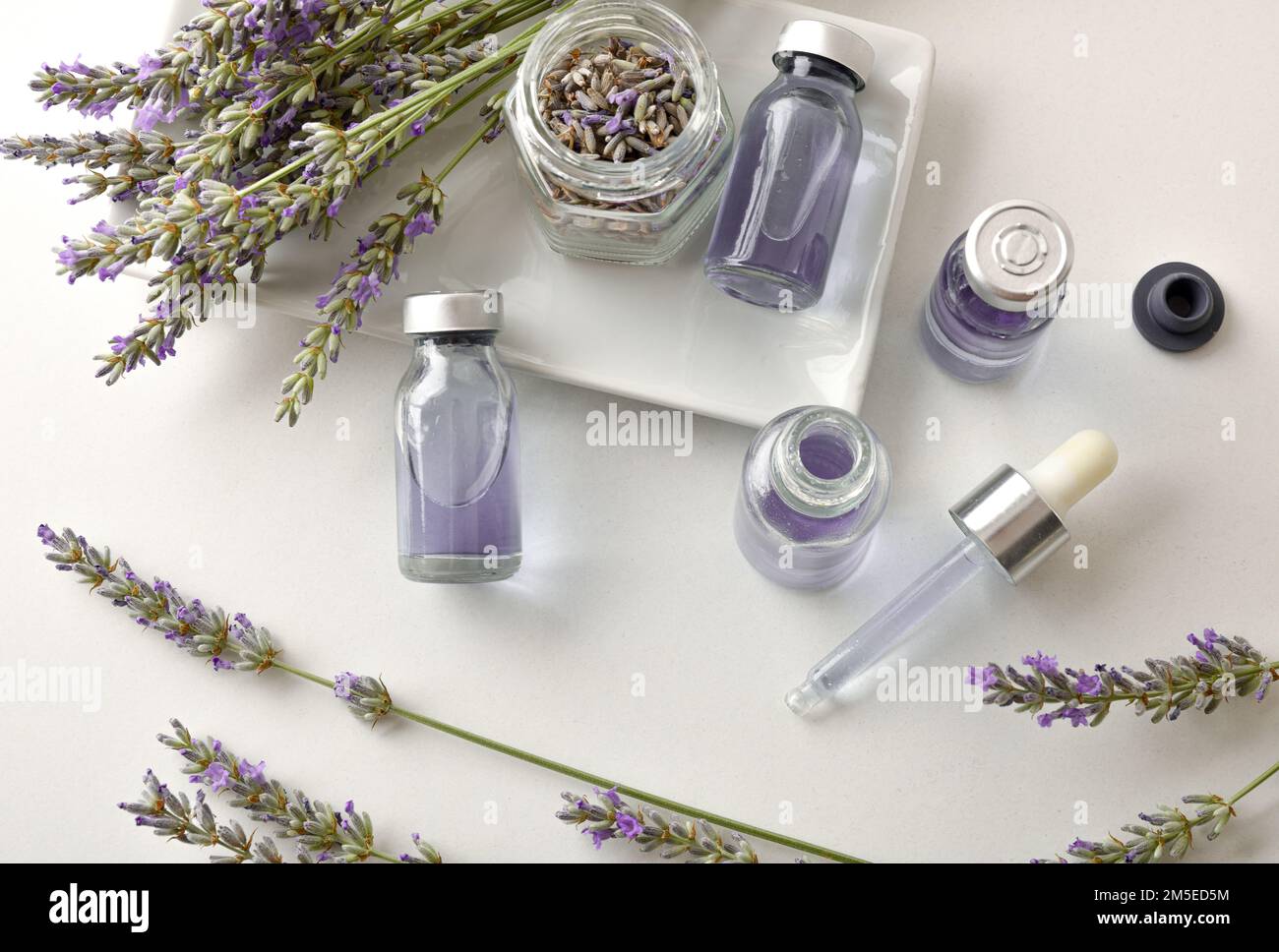 Preparation of lavender essences in bottles on white table with spikes in flower around. Top view. Horizontal composition. Stock Photo