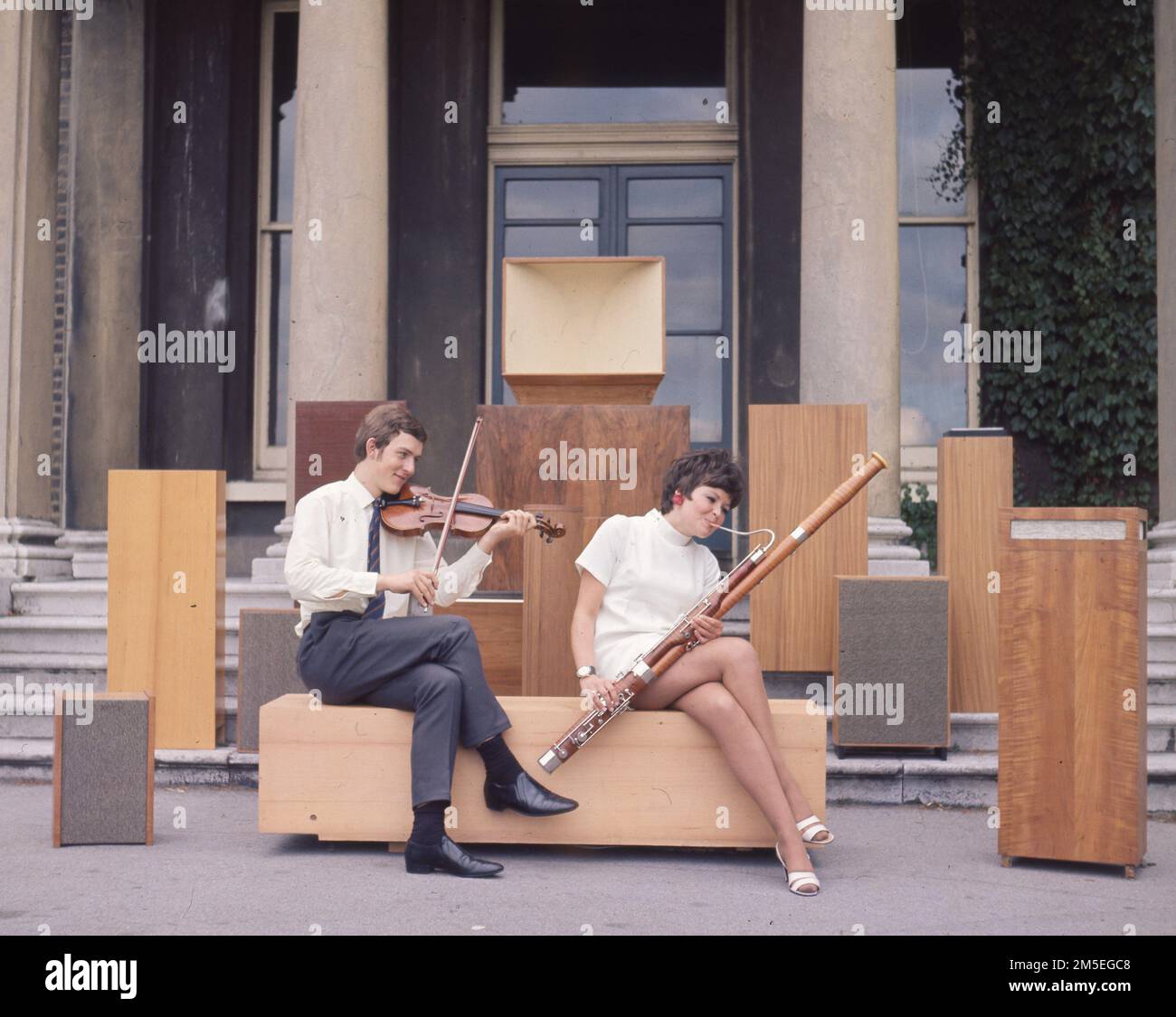 A violinist and female model poses with a basoon by vintage large speakers. c1970. Photo by Gilbert Adams    From The Gilbert Adams Collection - wholly owned by Tony Henshaw Stock Photo