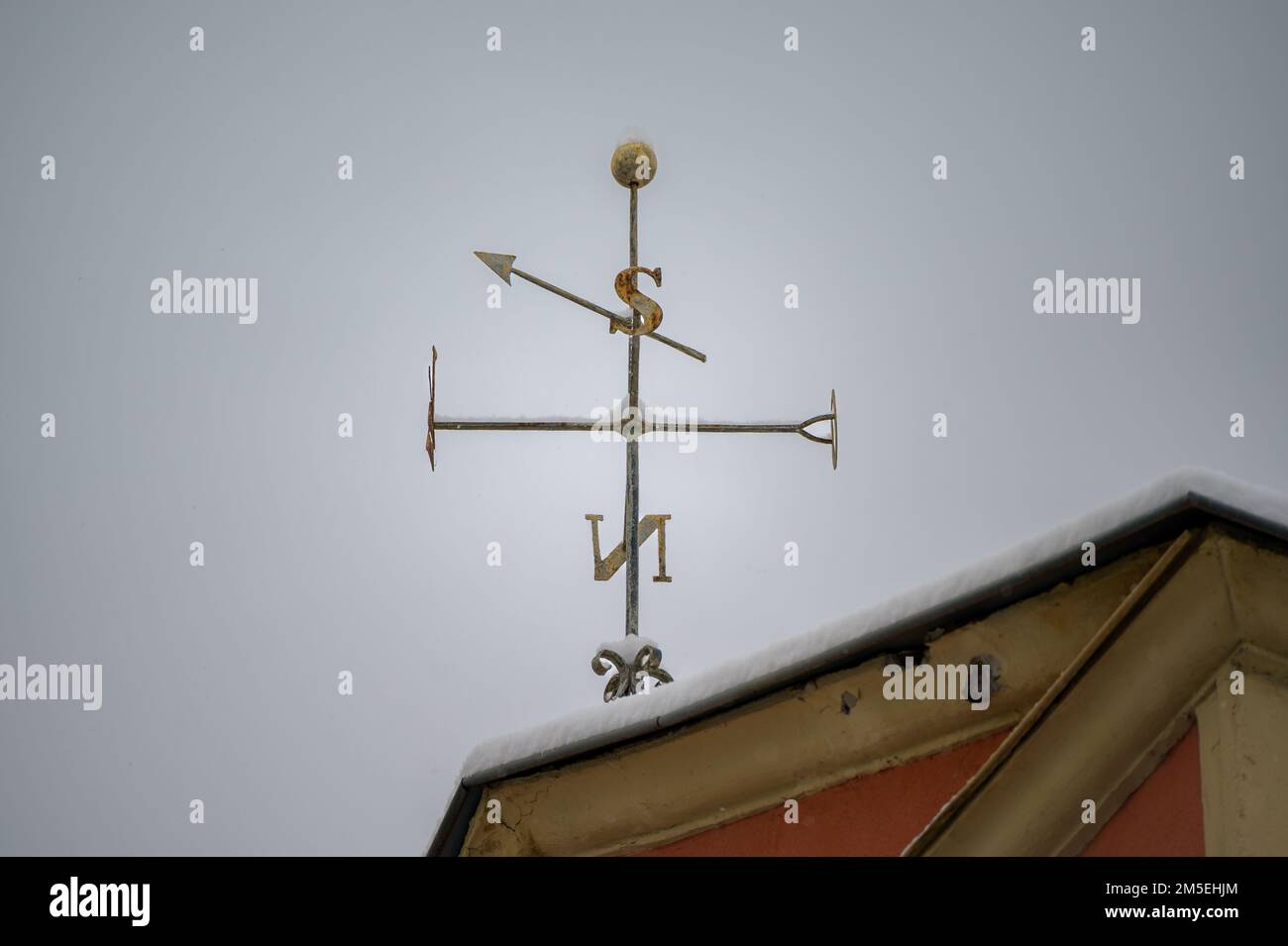 Golden weathervane with snow on top of old house roof with compass