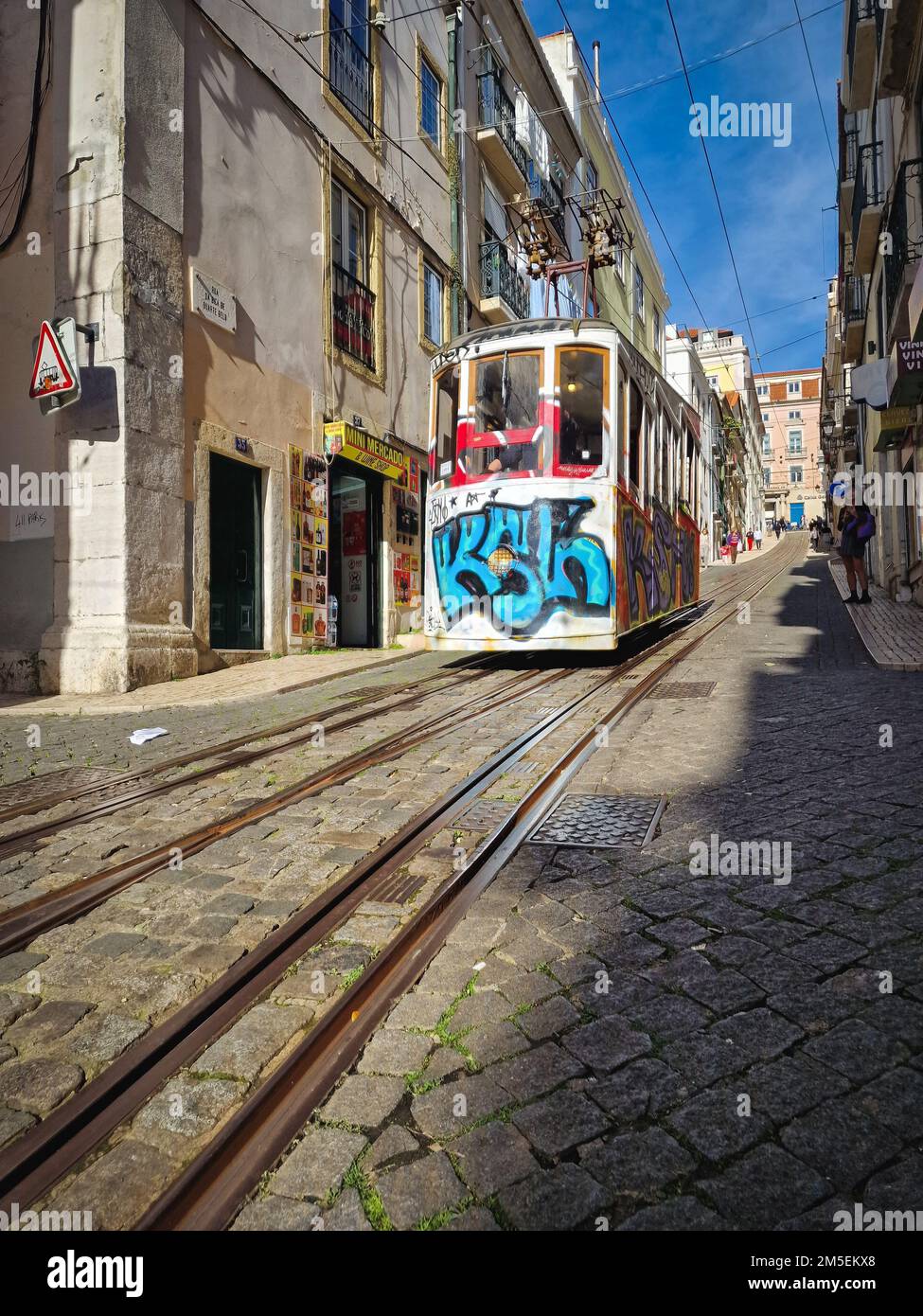 A vertical shot of a colored tram in a narrow street in Lisbon ...