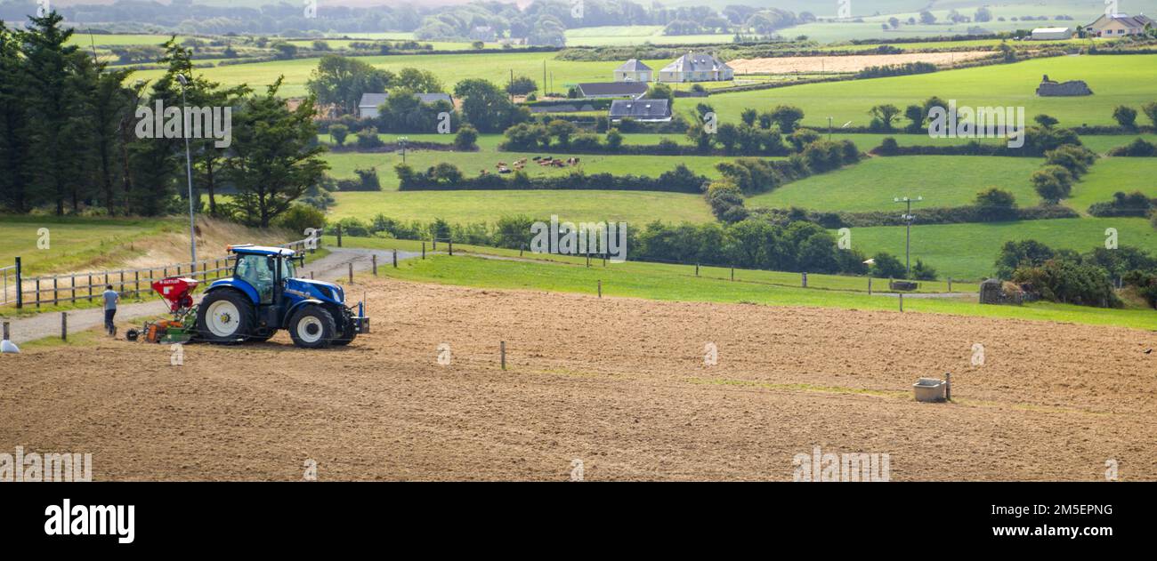 County Cork, Ireland, August 20, 2022. A blue tractor sows a plowed field on a summer day in Ireland. Agricultural work on an farm. Stock Photo