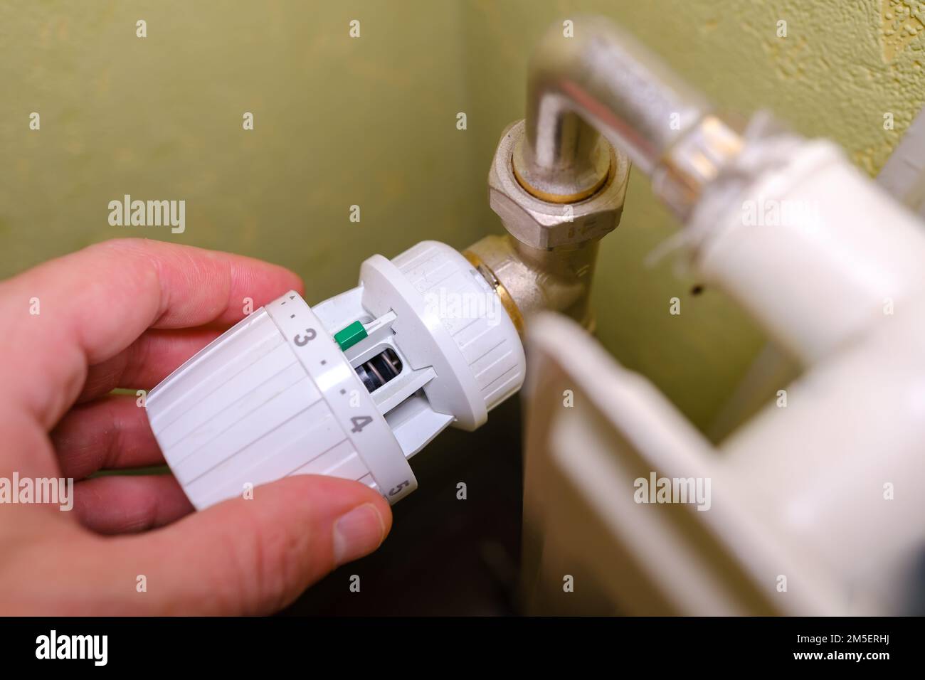 Rising heating costs in crisis, man regulates the temperature at home with the heating thermostat to save energy, close up Stock Photo