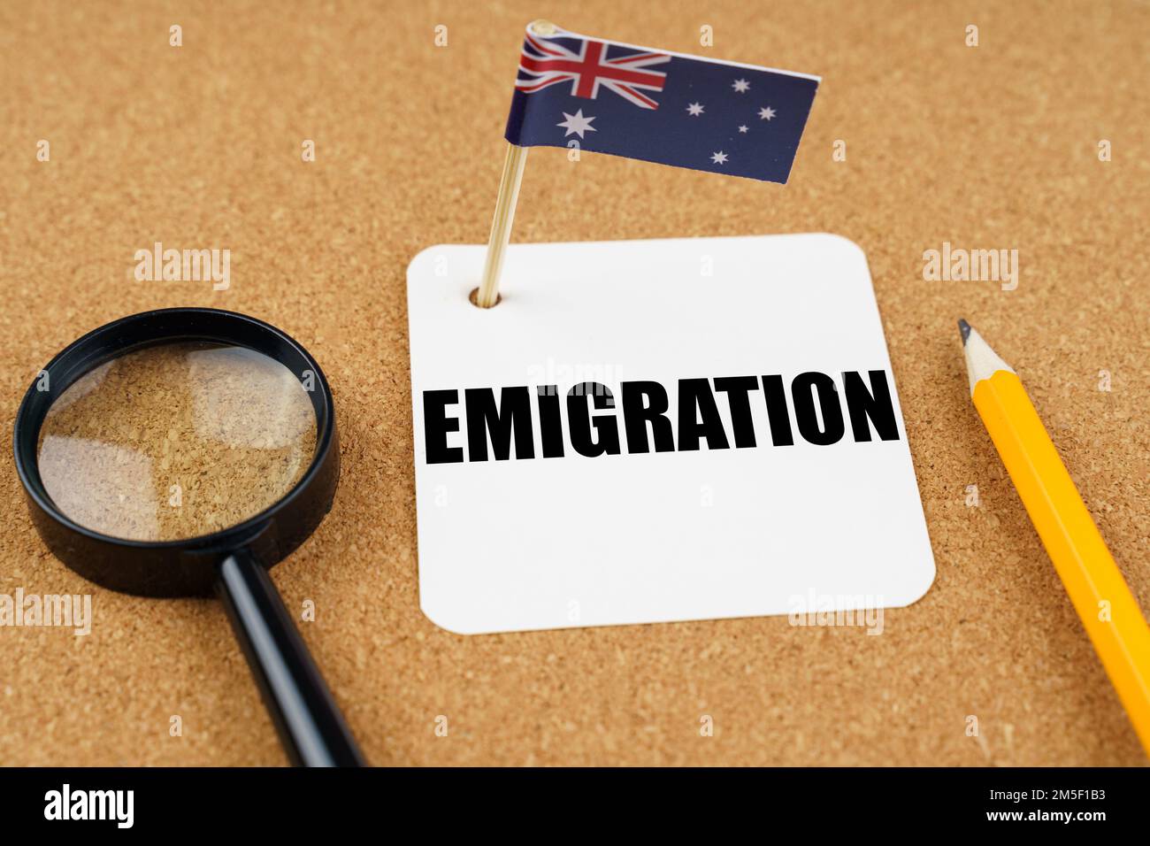 On the table is the flag of Australia, a pencil, a magnifying glass and a sheet of paper with the inscription - Emigration Stock Photo