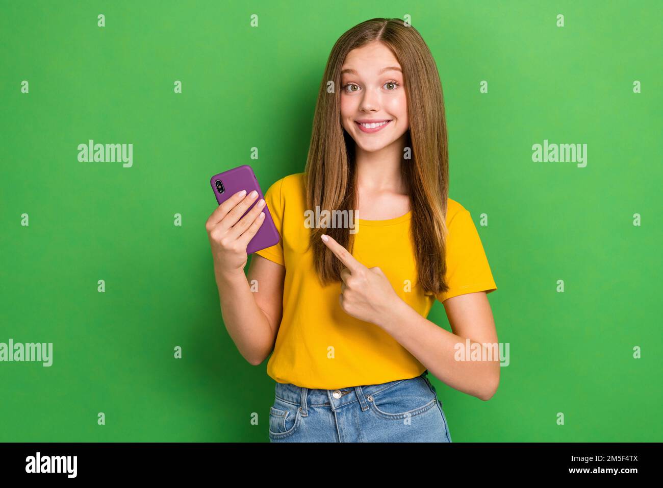 Photo of young satisfied teenager lady brown hair finger indicate her new apple iphone buy for sale cheap price isolated on green color background Stock Photo