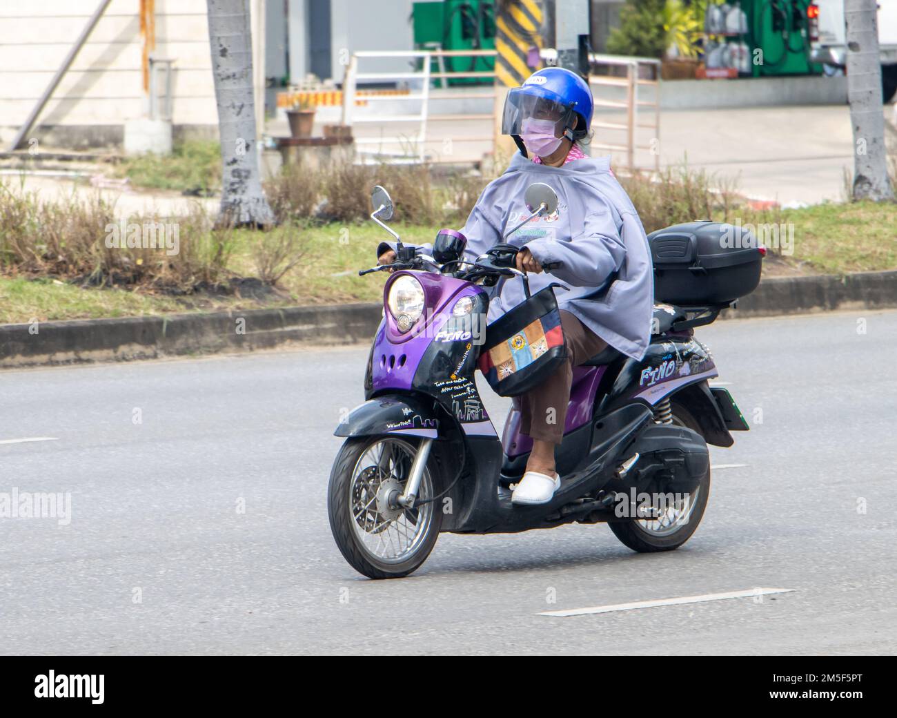 RATCHABURI, THAILAND, NOV 16 2022, A woman with her jacket turned to protect against the wind is riding a motorcycle Stock Photo