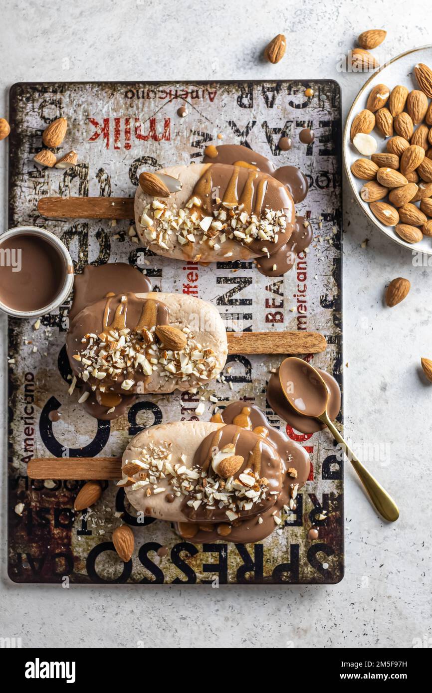 A few delicious homemade vegan ice cream bars or popsicles covered with chocolate and nuts top view, flat lay. Vertical Stock Photo