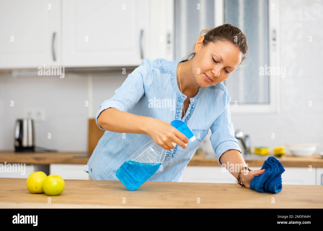Premium Photo  Smiling beautiful lady standing behind a modern kitchen  desk, dressed-up for housecleaning with detergents and rugs in front of her.