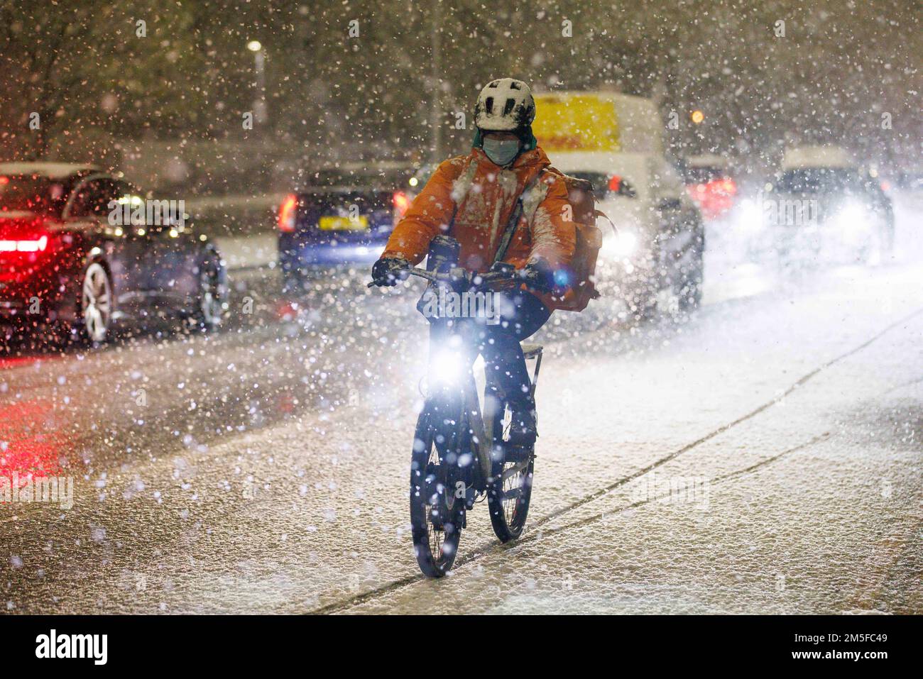 A cyclist braves the weather as snow falls in Stockwell, South West London, as an un-forecast cold snap covers the capital and much of the south east Stock Photo