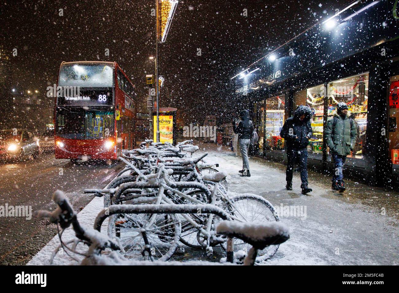 Snow falls on bicycles as a London bus passes by in Stockwell, South West London, as an un-forecast cold snap covers the capital and much of the south Stock Photo
