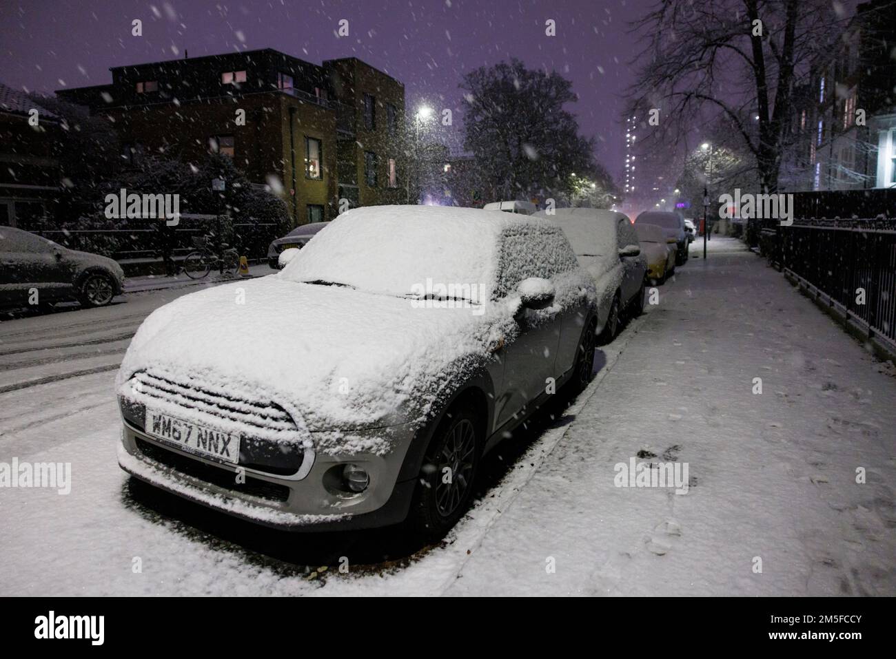 Snow falls on cars parked in Stockwell, South West London, as an un-forecast cold snap covers the capital and much of the south east of England with a Stock Photo