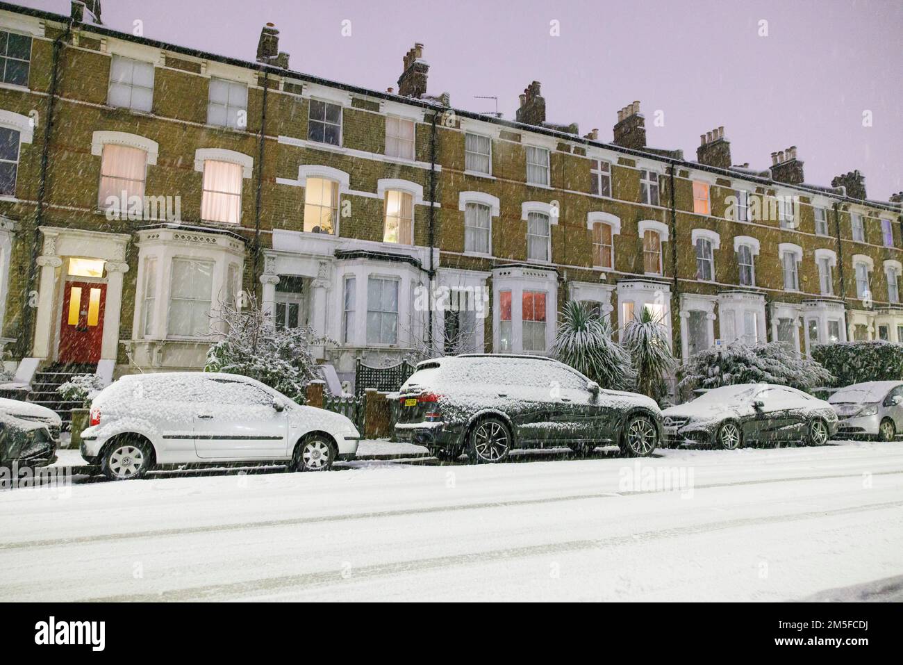 Snow falls on cars parked in Stockwell, South West London, as an un-forecast cold snap covers the capital and much of the south east of England with a Stock Photo