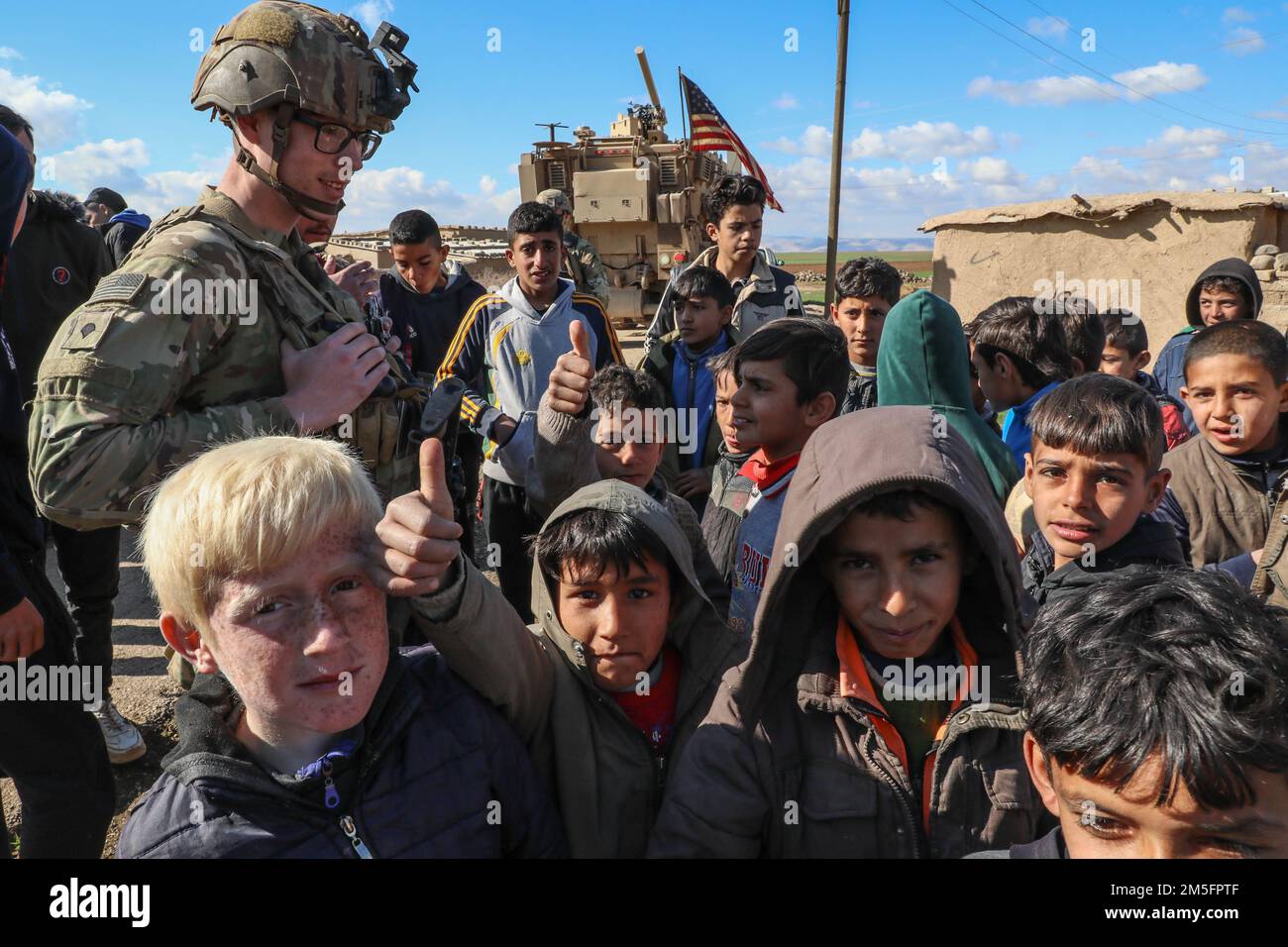 Children of a local village pose for a photo in Northeast, Syria on March 10, 2022 as a U.S. Soldier assigned to Comanche Troop, 1st Brigade, 4th Infantry Division, looks on. Combined Joint Task Force - Operation Inherent Resolve continues to advise, assist, and enable partner forces in designated areas of Syria to set conditions for long-term security. Stock Photo