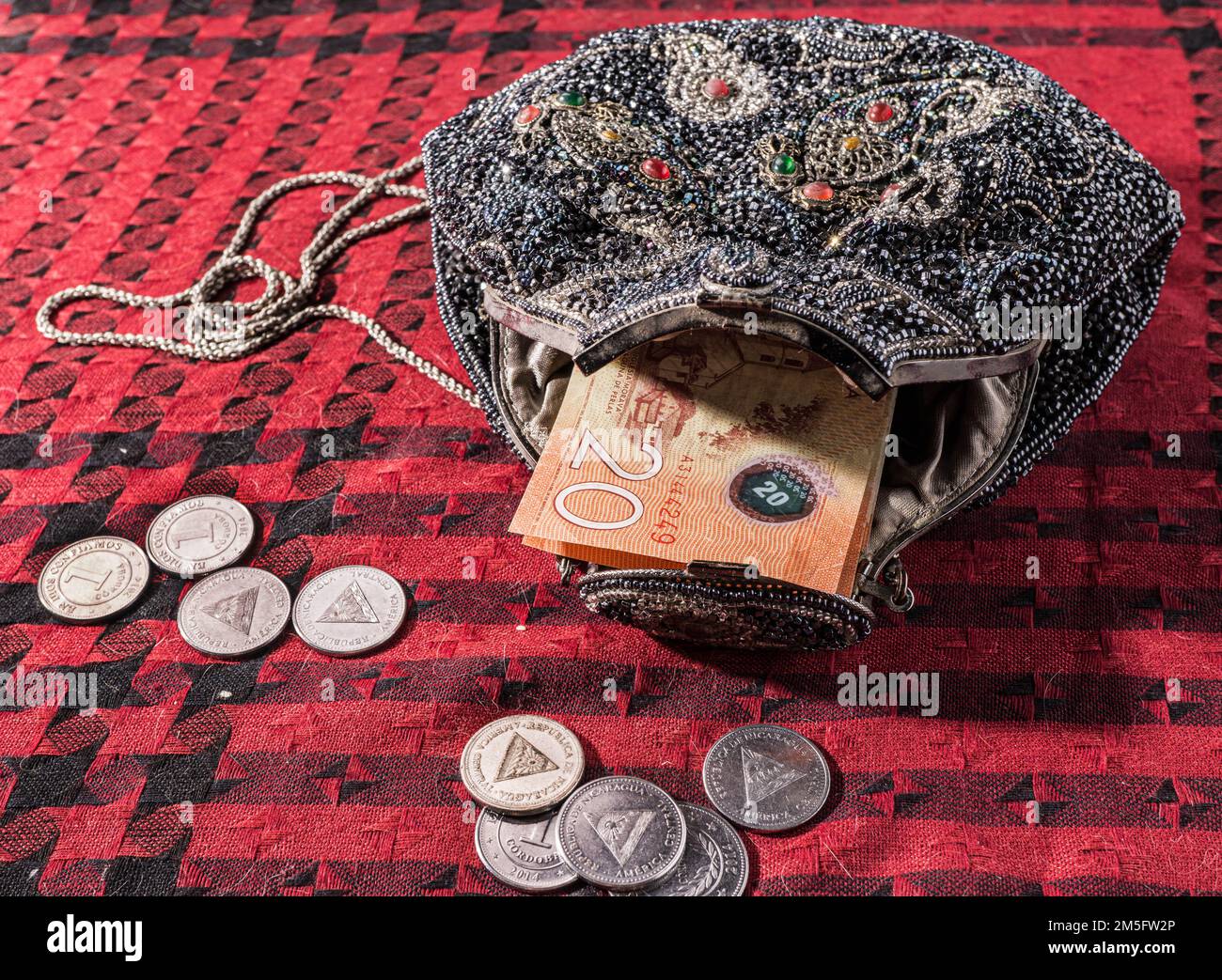 Beaded antique purse swallows Nicaraguan bills while surrounded by coins. Stock Photo