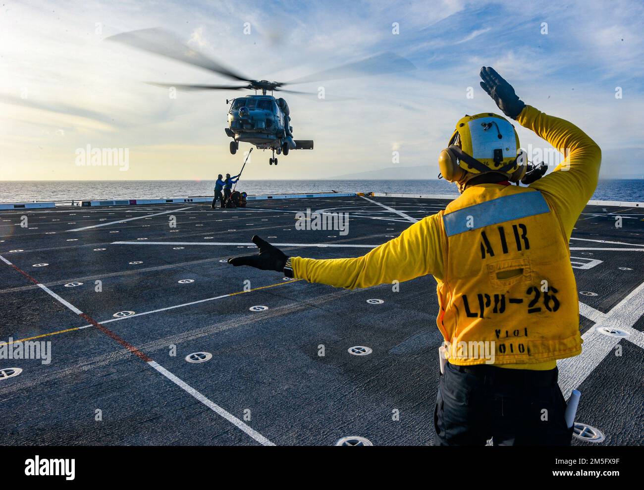 PACIFIC OCEAN (March 15, 2022) Aviation Boatswain’s Mate 3rd Class Kyro Lee, from Miami, assigned to amphibious transport dock ship USS John P. Murtha (LPD 26), directs an MH-60S Seahawk helicopter attached to the “Easy Riders” of Helicopter Maritime Strike Squadron (HSM) 37 to move into position during a vertical replenishment-at-sea (VERTREP), March 15.  John P. Murtha is underway conducting routine operations in U.S. 3rd Fleet. Stock Photo