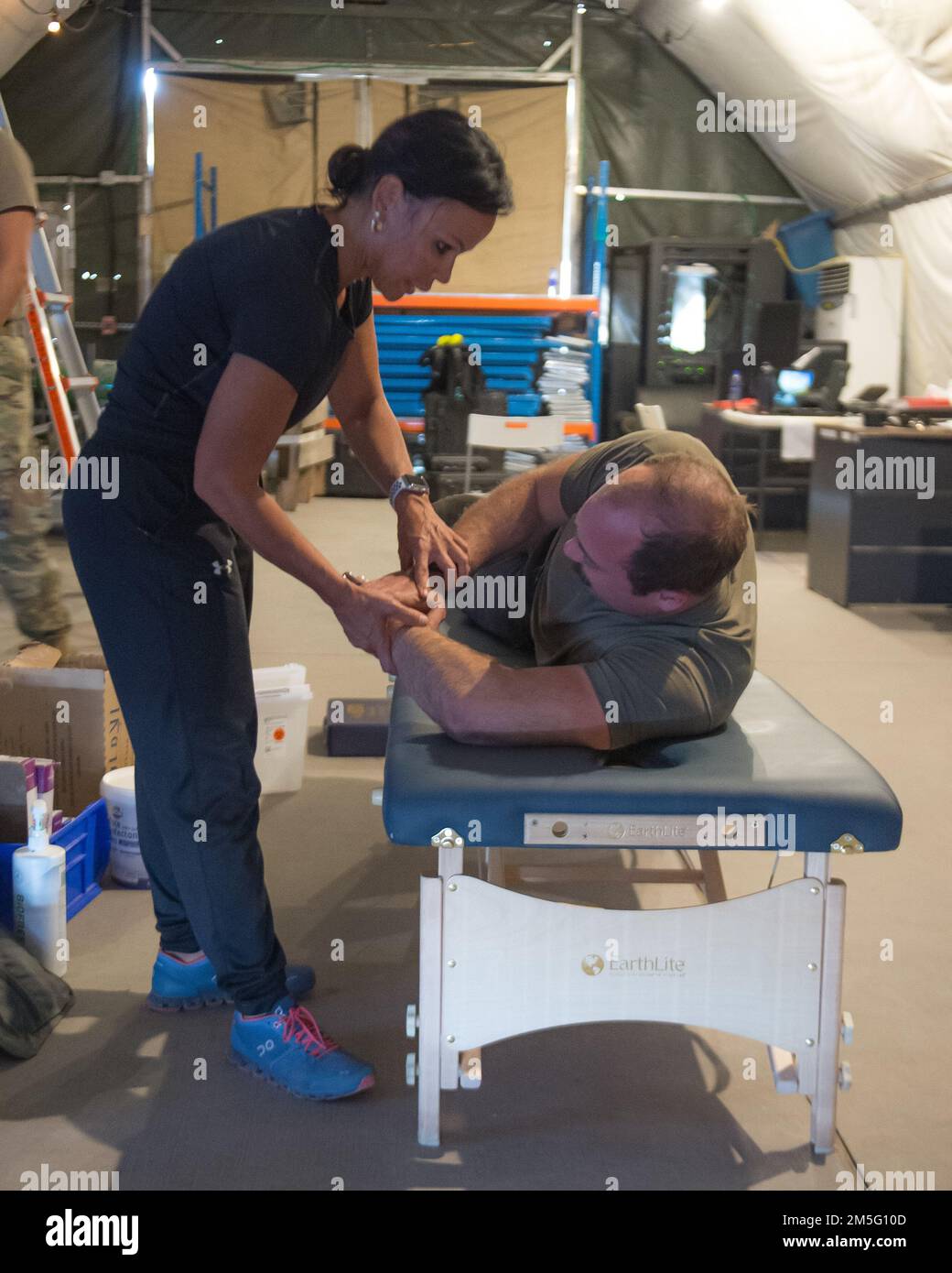 Lt. Col. Denise Lemon, a physical therapist, 380th Expeditionary Medical Group, Al Dhafra Air Base, stretches a patient from the 1st Fighter Wing, Joint Base Langley-Eustis, Virginia, at a pop-up treatment area on the flight line here, on March 16, 2022. The physical therapy team mobilizes to treat Airmen from as many units as possible on a weekly basis, providing Airmen an opportunity to seek relief in the middle of their workday. Stock Photo
