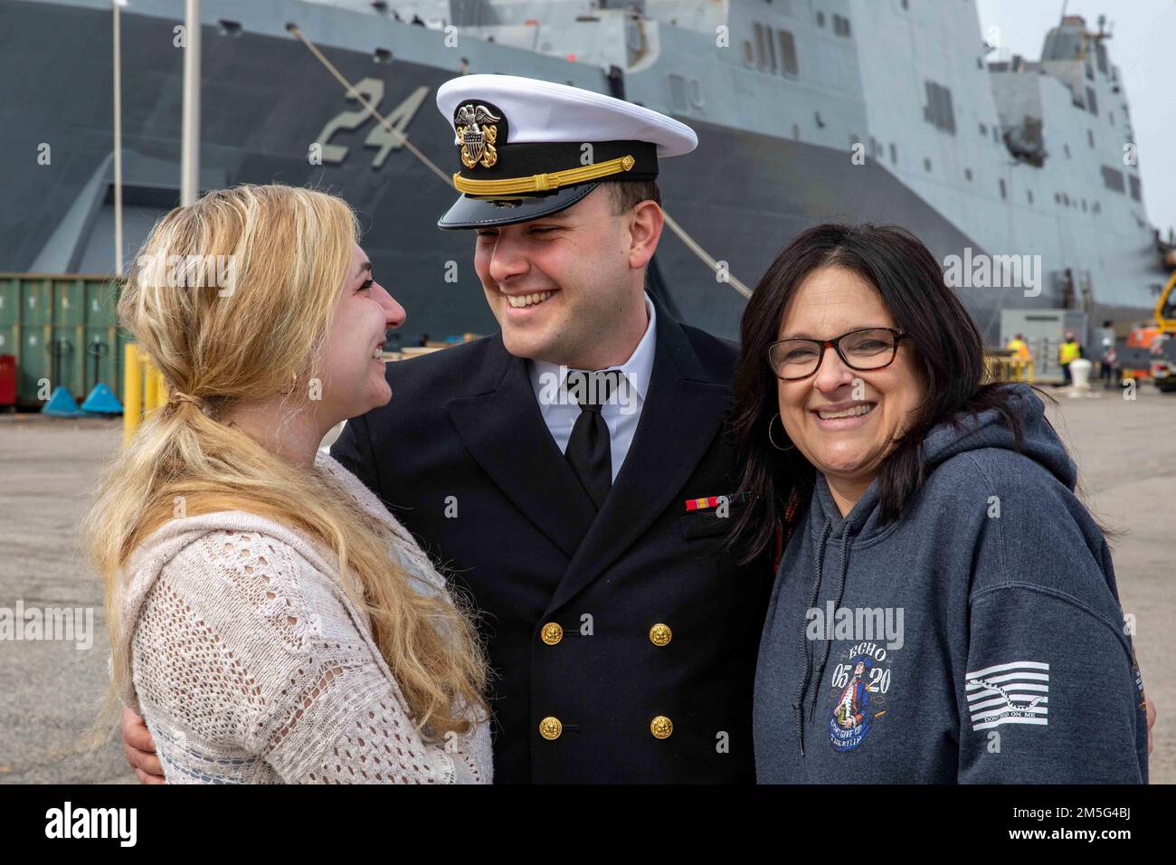 220316-N-PC065-1263 ATLANTIC OCEAN – Lt. j.g. Matthew Bonamassa, assigned to the San Antonio-class amphibious transport dock ship USS Arlington (LPD 24), poses for a photo with his mother, right, and girlfriend prior to deploying from Naval Station Norfolk, Virginia, March 16, 2022. Arlington is operating in the Atlantic Ocean in support of naval operations to maintain maritime stability and security in order to ensure access, deter aggression and defend U.S. allied and partner interests. Stock Photo