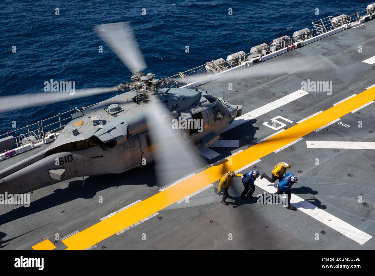 220316-N-TF178-1071    PACIFIC OCEAN (March 16, 2022) – Sailors exit the rotor arc of an MH-60S Sea Hawk, assigned to Helicopter Sea Combat Squadron (HSC) 6, after removing tie-down chains on the flight deck aboard amphibious assault ship USS Makin Island (LHD 8), March 16. Makin Island is underway conducting routine operations in U.S. 3rd Fleet. Stock Photo