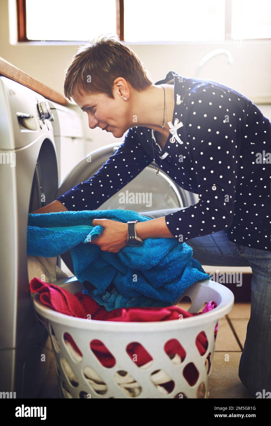 All washed and ready for drying. a cheerful young woman taking washing out of a washing machine at home. Stock Photo
