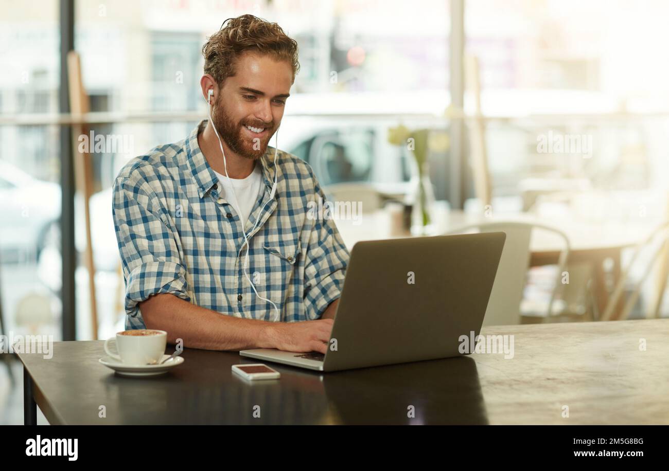 Its all about staying positive. a young man with earphones using a laptop in a cafe. Stock Photo