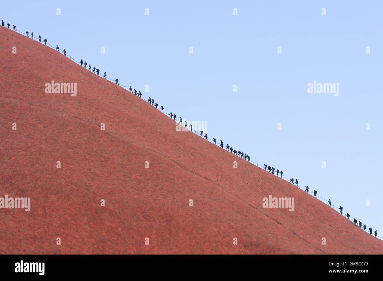 A long queue of people climbs the steep red rock face of Uluru (Ayers Rock), Australia Stock Photo
