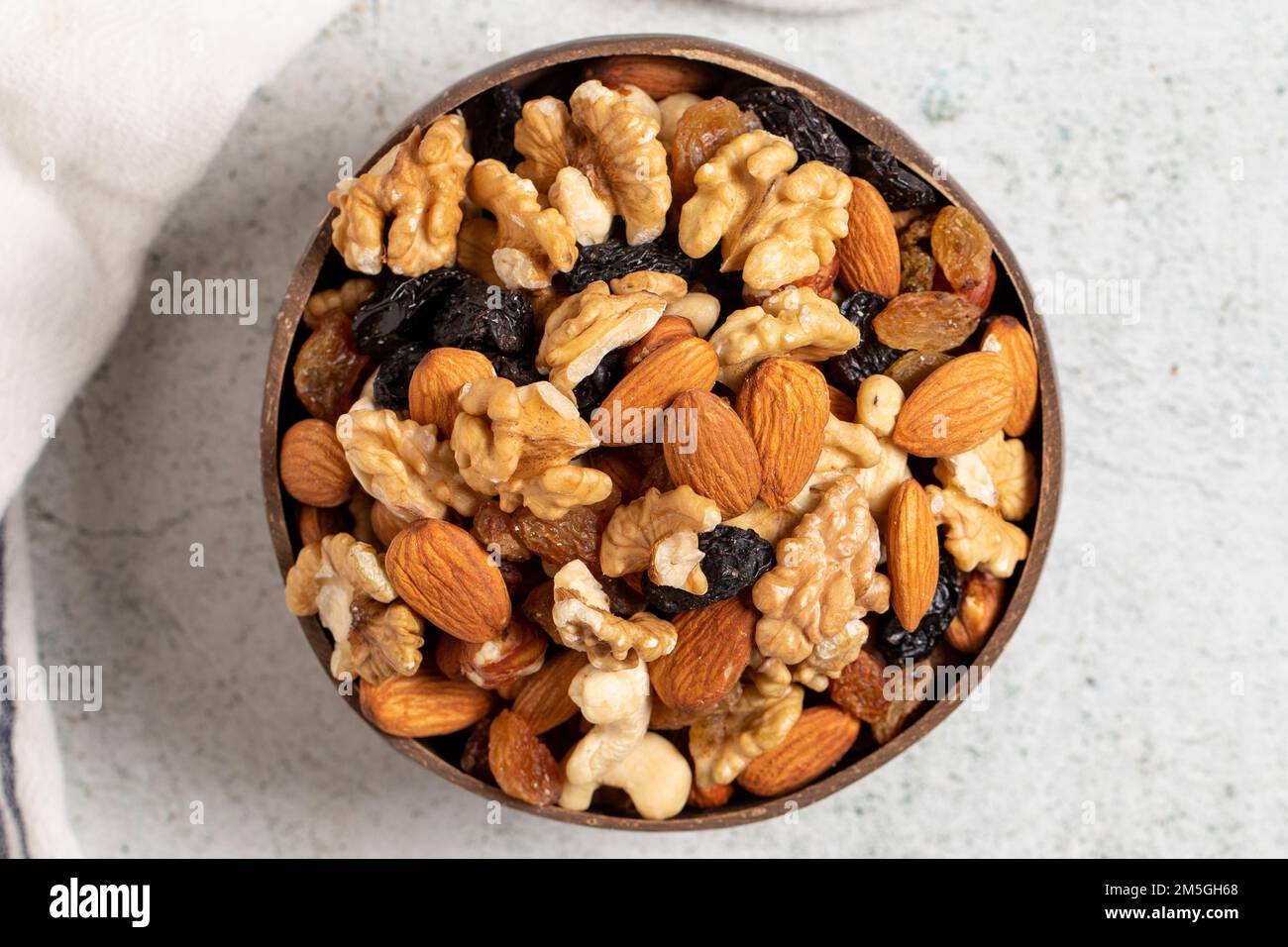 Raw mixed nuts on gray background. Walnuts, almonds, hazelnuts and raisins in a coconut bowl. Top view Stock Photo