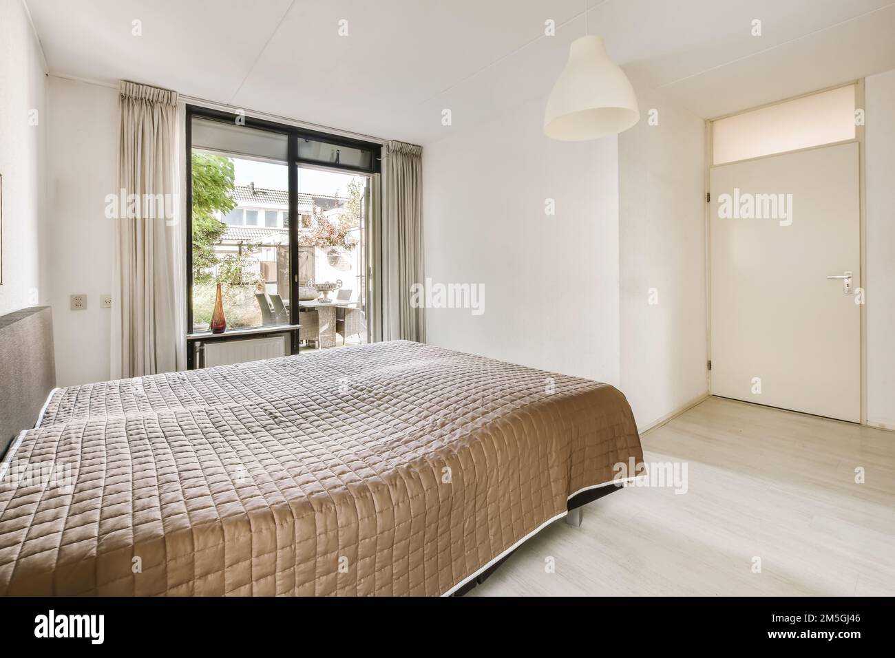 a bedroom with a bed and a large window looking out onto the street in front of the room to the outside Stock Photo