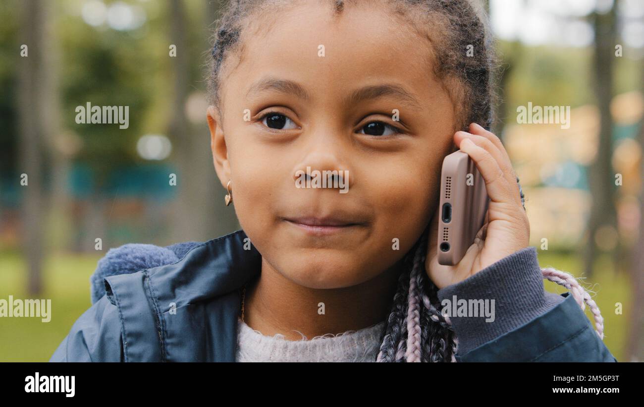 Little ethnic girl talking on mobile phone outdoors portrait funny multiracial child answer telephone call small African American baby kid daughter Stock Photo