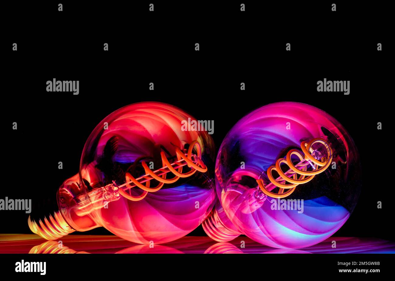 Colourful patterns reflect within a pair of clear glass round shaped lightbulbs, photographed against a black background Stock Photo