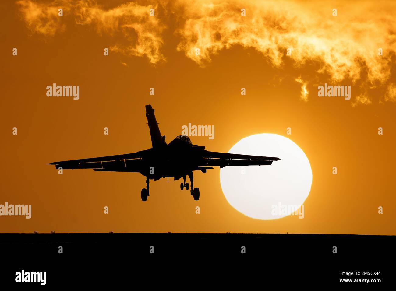 Fighter jet landing at sunset with orange sky and large setting sun after a combat mission. Tornado Fighter Bomber Stock Photo
