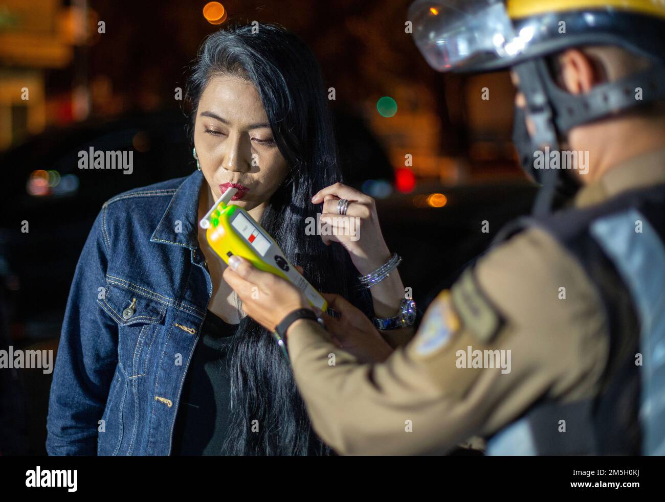 A thai police officer takes a driver through an alcohol tests using a breathalyzer at Check point in Chiang Mai. The Center for Prevention and Reduction of Road Accidents has been established during the New Year's Festival 2023, the 7-day intensive control period from 29 December 2022 to 4 January 2023. More than 50,000 police officers are to set up checkpoints to facilitate traffic laws and take care of the safety of people. They will work throughout the festival without holidays, focusing on 4 charges according to government policy: driving while intoxicated, driving too fast, and not wearin Stock Photo
