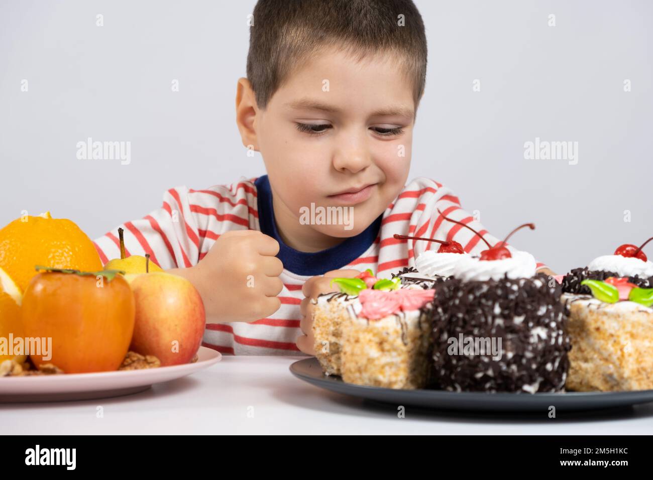 5 year old cute boy sits in front of fruits and cakes and chooses what