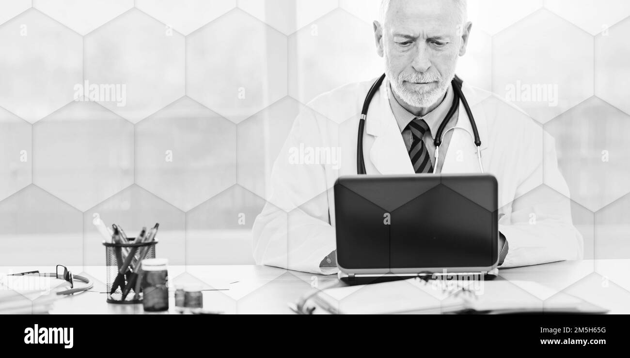 Senior doctor using laptop in medical office, geometric pattern Stock Photo
