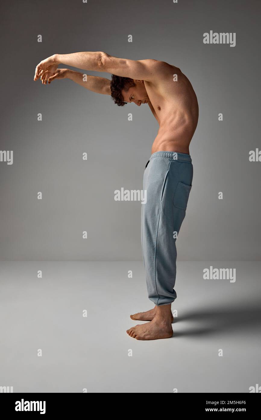 Round back. Healthy, strong back, spine. Muscular man posing shirtless, in pants over grey studio background. Stretching. Men's health and beauty Stock Photo