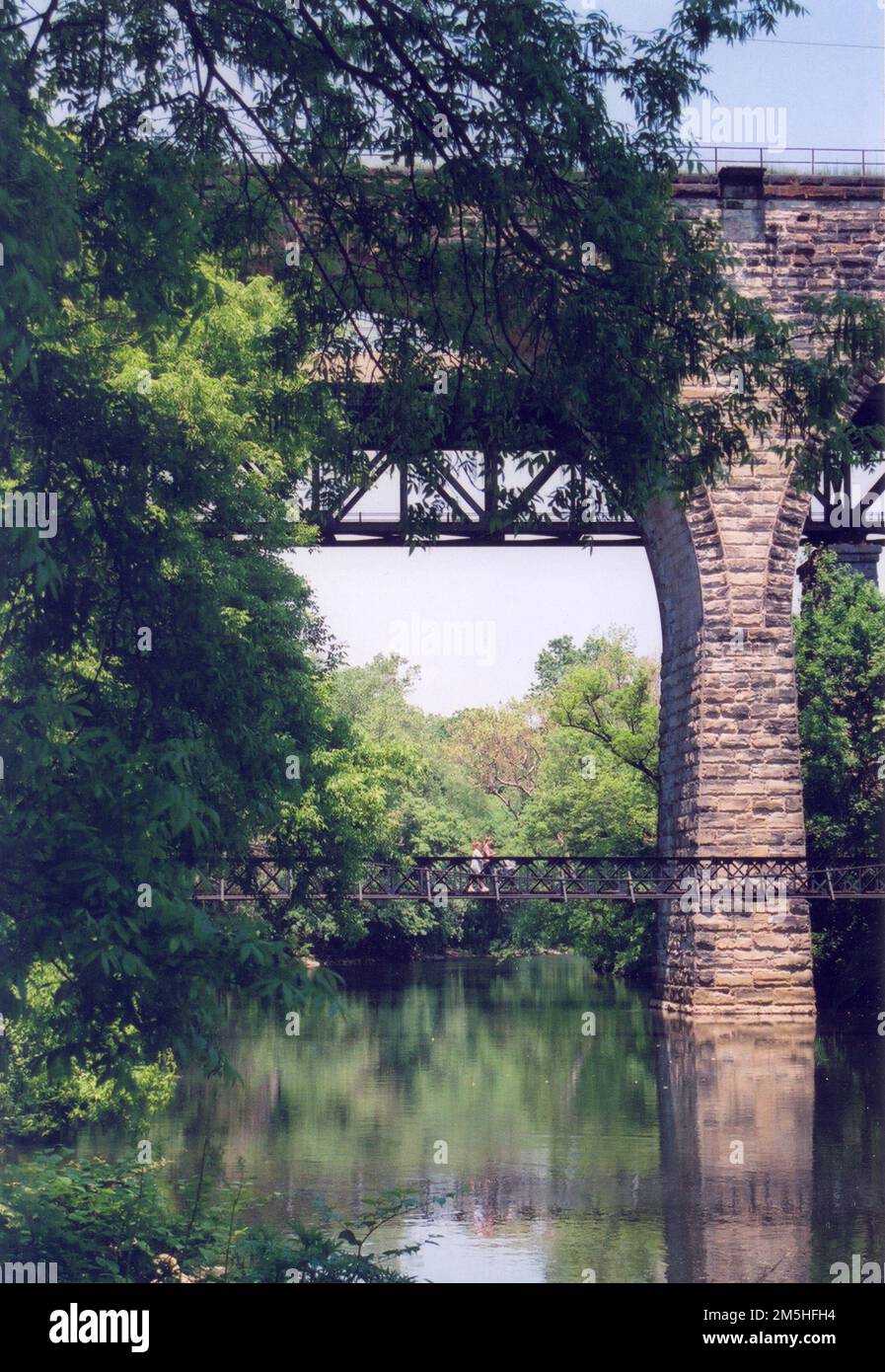 Brandywine Valley Scenic Byway - Bridge at Brandywine River Park. In Brandywine River Park, people stroll over the lower pedestrian bridge while the upper stone bridge is reflected in the clear water of the Brandywine River. Location: Brandywine River Park, Wilmington, Delaware Stock Photo