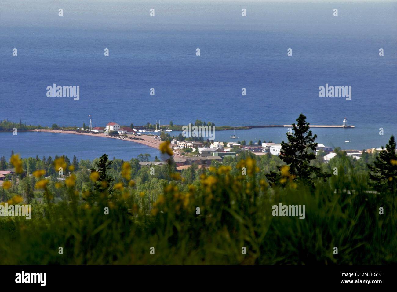 Gunflint Trail Scenic Byway - View of Grand Marais from Sawtooth Mountain Ridgeline. The small town of Grand Marais (population 1100) lies 1000 feet below this overlook perched on a steep hillside. The natural and man-made breakwaters and two lighthouses of Grand Marais gracefully embrace the entrance to the harbor. The deep blue of Lake Superior makes up the background. Grand Marais, Minnesota (47.746° N 90.333° W) Stock Photo