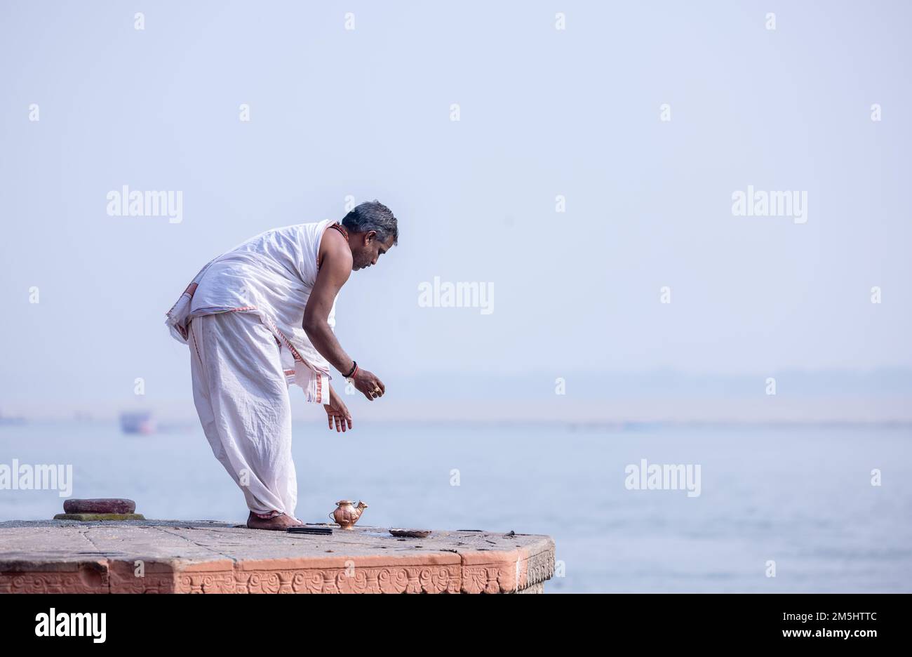 Varanasi, India: Portrait of Unidentified Indian sadhu baba worshiping lord sun in traditional white dress on ghat near river ganges in varanasi city. Stock Photo