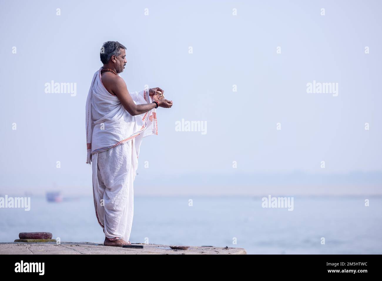 Varanasi, India: Portrait of Unidentified Indian sadhu baba worshiping lord sun in traditional white dress on ghat near river ganges in varanasi city. Stock Photo