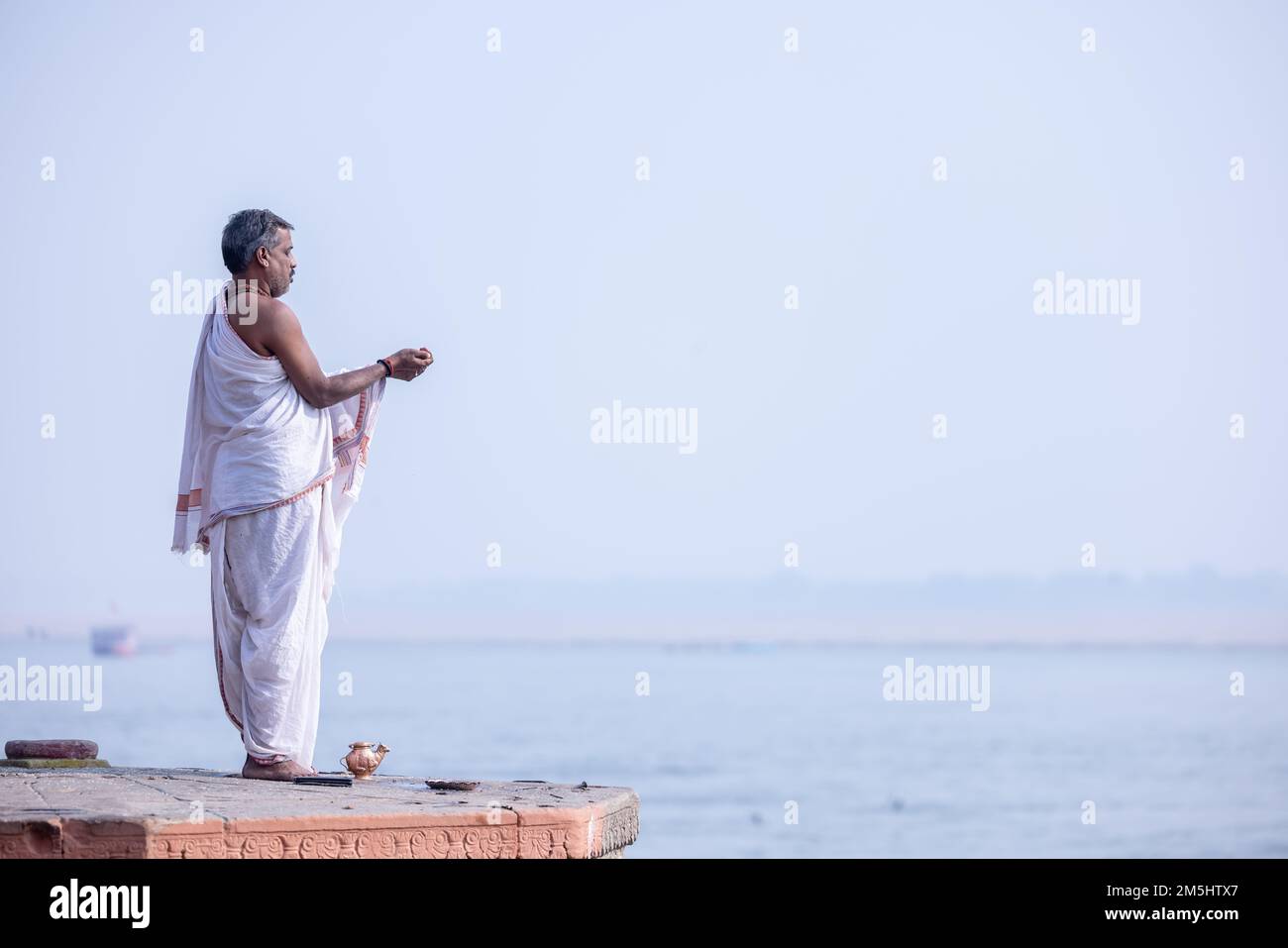 Varanasi, India: Portrait of Unidentified Indian sadhu baba worshiping lord sun in traditional white dress on ghat near river ganges in varanasi city. Stock Photo